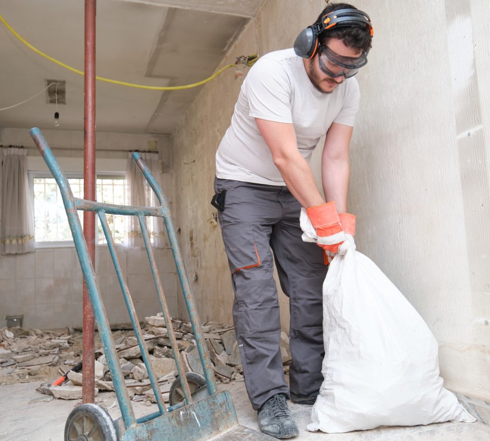 Builder collecting construction debris in a bag, and carrying in a hand trolley. House renovation.