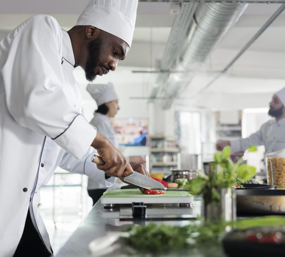 Head chef in restaurant professional kitchen preparing delicious meal. Food industry worker cutting fresh and organic vegetables while cooking gourmet dish for dinner service